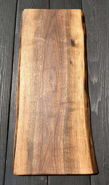 Single 22-inch long and 8-12-inch wide live-edge black walnut charcuterie board with black wood panel background